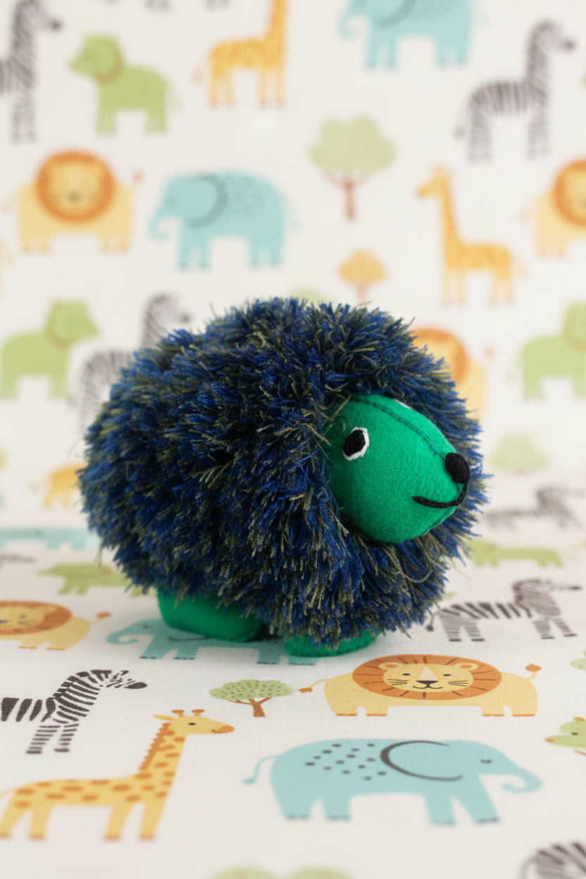 A small plush hedgehog toy with a shaggy dark blue and black fur-like body and a bright green face, nose, and feet, photographed on a clean white background.