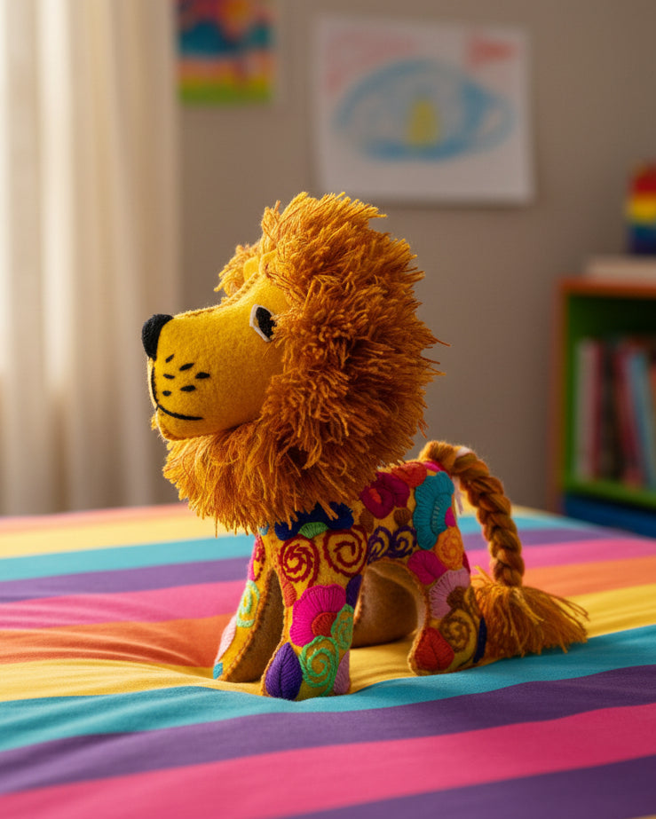 A handmade plush lion toy with a golden-yellow face and fluffy orange-brown mane, wearing a vibrant, multicolored patterned dress, set against a plain white background.